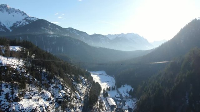Aerial footage of the mountains with snow and the forest with footbridge, 4k