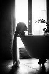 A beautiful woman with gorgeous long blond hair is relaxing in the bath. Silhouette of a woman in profile lying in the bathroom.