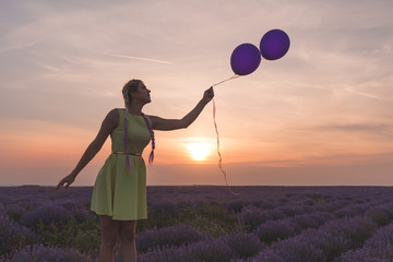 A beautiful model with long braids stands in a lavender field. Holds two balloons in his hands. Sunset in the background.