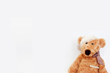 soft brown toy bear sick with a bandage on his head and a medical thermometer