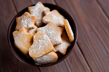 homemade cookies in the shape of hearts and stars on the table in a bowl on a brown wooden background