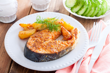 Salmon steak baked with mustard and potatoes on a white plate, horizontal