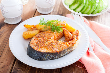 Salmon steak baked with mustard and potatoes on a white plate, horizontal