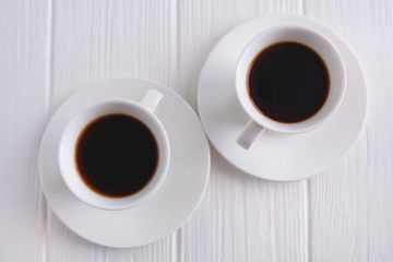 two cups of black coffee on white wooden background, top view