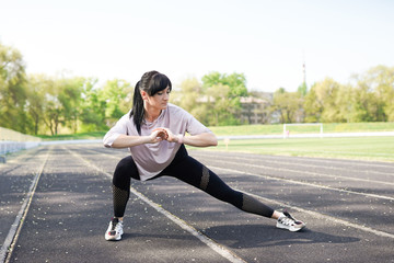 Young fitness girl doing stretching on the stadium. Summer sport activity. Green stadium background with copy space