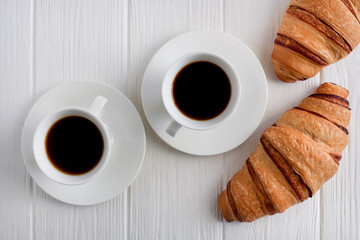 Fresh croissants on a white background and black coffee. Breakfast. Top view