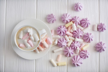 A cup of cappuccino with pastel colored marshmallows on a white background with lilac meringue, top view