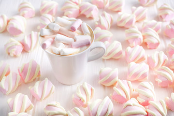 Obraz na płótnie Canvas cappuccino or cocoa with marshmallow in a white cup on the background of marshmallow on a white table in bulk