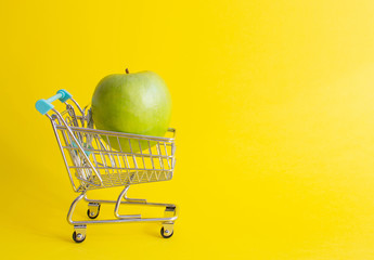 Mini shopping trolley on yellow background with fruits, copy space, consumer concept, summer time