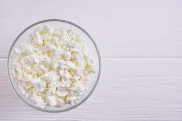 Fresh cottage cheese in a bowl on a white wooden table top view, copy space