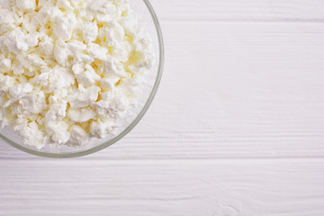 Fresh cottage cheese in a bowl on a white wooden background, top view, copy space