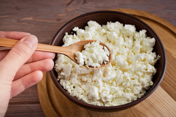 woman's hand holding a wooden spoon with curd on a brown table and plank