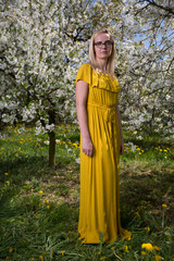  A beautiful, sunny, calm, spring day. Young woman in orchard amid blossoming cherry trees. Relax in the greenery away from the city in the countryside.