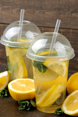 Homemade lemonade with mint and lemon in plastic glasses on a brown background. Refreshing lemonade drink.