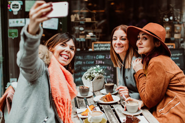 .Group of young friends drinking coffee with cakes in an outdoor cafe in Porto, Portugal. Talking pictures together with their phone. Lifestyle. Travel photography