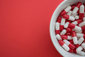 Bowl of drugs pills capsules on red color background