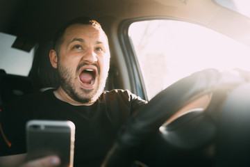 Young man sitting in his car screaming distracted by smartphone