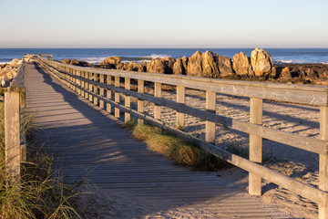 Wooden path with fence to the beach. Walkway on seashore in the morning. Travel and walk concept. Camino de Santiago landscape. Atlantic Ocean coast in Portugal. Wooden pier in perspective. 
