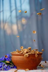 falling sugar cornflakes in a ceramic bowl close-up top view. light breakfast scattered on the table with blue flowers close-up against the window. food fast cooking. healthy food, diet. Vertical