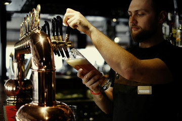 Pouring beer. Cropped image of smiley bartender poring beer to the mug