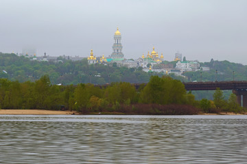 Scenic morning view of Dnipro River, green hills with ancient Kyiv Pechersk Lavra. Mysterious foggy spring landscape. Kyiv, Ukraine