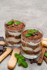 Classic tiramisu dessert in a glass and savoiardi cookies on concrete background