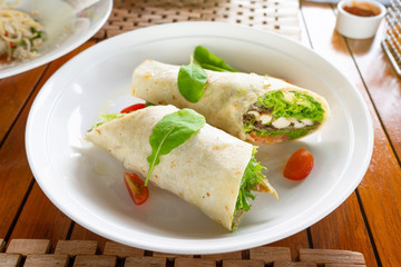 Tortilla wrap with chicken meat and vegetables on traditional dish toping with spinach.