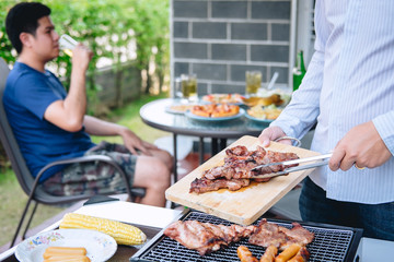 Group of friends Two young man enjoying grilled meat and raise a glass of beer to celebrate the holiday festival happy drinking beer outdoors and enjoyment at home