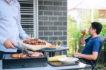 Group of friends Two young man enjoying grilled meat and raise a glass of beer to celebrate the holiday festival happy drinking beer outdoors and enjoyment at home