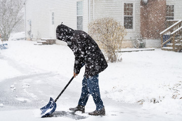 Young man in winter coat cleaning shoveling driveway street from snow in heavy snowing snowstorm with shovel by residential house and snowflakes falling © Andriy Blokhin