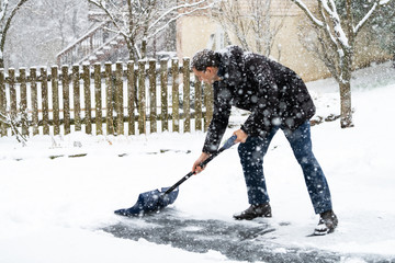 Man in winter coat cleaning shoveling driveway street in heavy snow storm with shovel and...