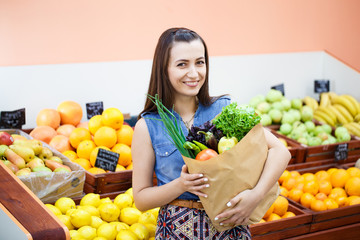 Obraz premium Beautiful young girl with a paper bag with shopping in a vegetable store