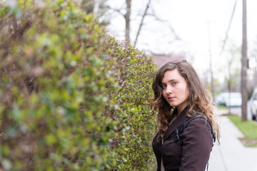 Young woman closeup portrait on sidewalk street in Washington DC, USA United States during spring with hedge green bush in University Heights residential area