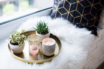 Cozy real home decoration, burning candles on golden tray with pillow on white faux fur on...