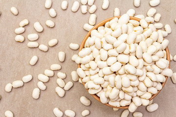 Dry lima beans in ceramic bowl on stone background, top view, wallpaper, close up.
