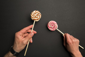 cropped view of man and woman holding sweet lollipops on wooden sticks on black background