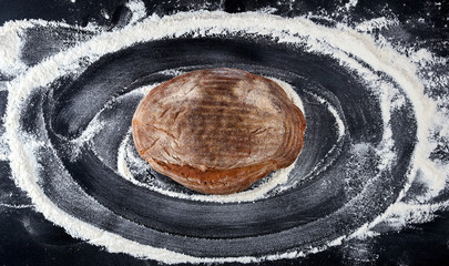 baked bread and white wheat flour scattered on a black table