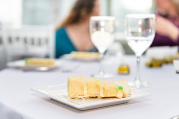 Table with glasses of water in restaurant or wedding reception white table tablecloth plates with yellow cake slices and background of guests eating