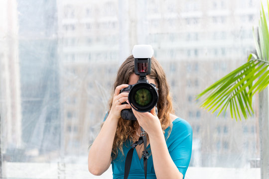 One young wedding photographer woman in dress standing with camera external flash taking picture photo and lens covering face
