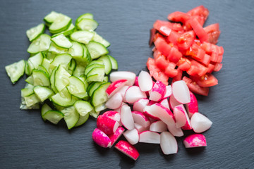 Sliced fresh cucumbers, tomatoes and red radishes on a black background. Cooking salad from vegetables. The concept of healthy eating, vegetarianism.