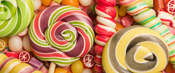 Panoramic shot of bright round and swirl lollipops on fruit caramel candies