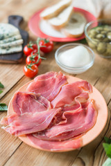 Sliced jamon on a plate on a wooden background and other various products. Cooking snacks in the kitchen.