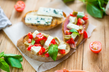 Traditional Italian bruschetta with blue cheese, feta, tomatoes, basil leaves, jamon on a wooden background.