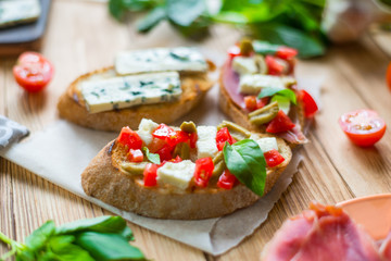 Traditional Italian bruschetta with blue cheese, feta, tomatoes, basil leaves, jamon on a wooden background.