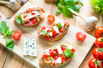 Traditional Italian bruschetta with blue cheese, feta, tomatoes, basil leaves, jamon on a wooden background.