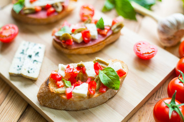 Toasted ciabatta, a cheese sandwich with mold, tomatoes, basil on a wooden background.