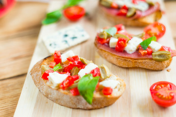 Traditional Italian bruschetta with blue cheese, feta, tomatoes, basil leaves, jamon on a wooden background.