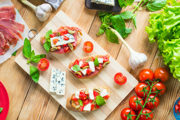 Traditional Italian bruschetta with blue cheese, feta, tomatoes, basil leaves, jamon on a wooden background.