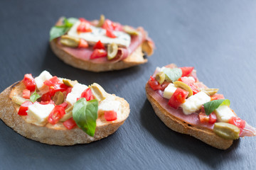 Traditional Italian bruschetta with blue cheese, feta, tomatoes, basil leaves, jamon on black stone background.