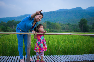 Happy Mother and her child play outdoors having fun, and pointing at something in the Green rice field.